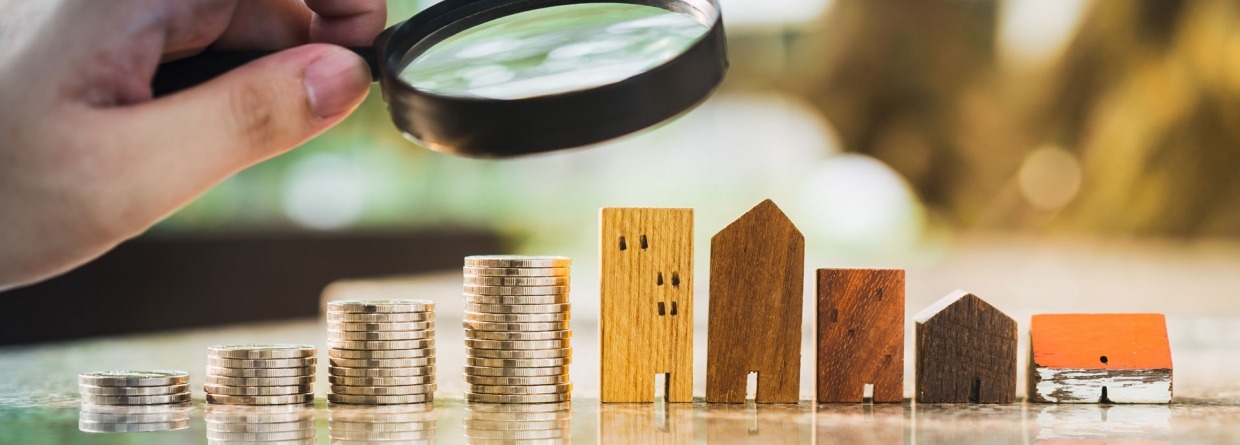 hand met een vergrootglas boven een rij huizen en geld