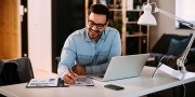 Jonge zakenman die thuis werkt met laptop en papieren op bureau